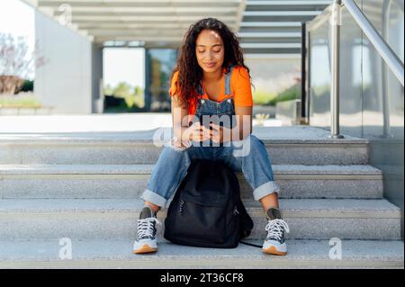 Happy student using smart phone on steps in campus Stock Photo