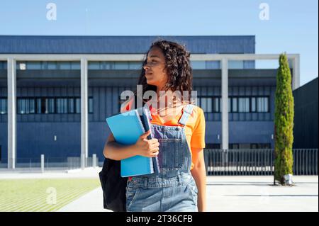 Student holding spiral notebooks and walking in front of building Stock Photo