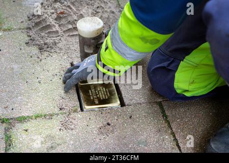 Wiesbaden, Germany - October 17, 2023: A bricklayer lays Stolpersteine on a pavement in the city center of Wiesbaden, Germany. A Stolperstein (literally 'stumbling stone') is a concrete cube provided with a brass plate inscribed with the name and life dates of victims of Nazi extermination. Stock Photo