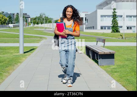 Happy student holding books and walking in campus Stock Photo