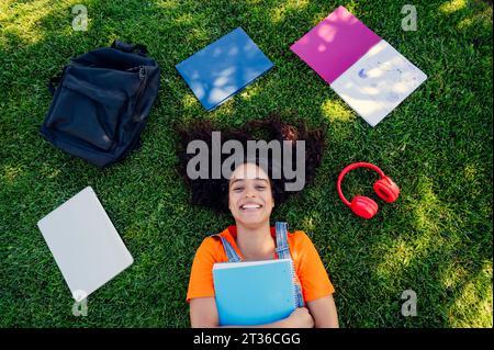 Smiling student lying on grass with spiral notebooks in campus Stock Photo