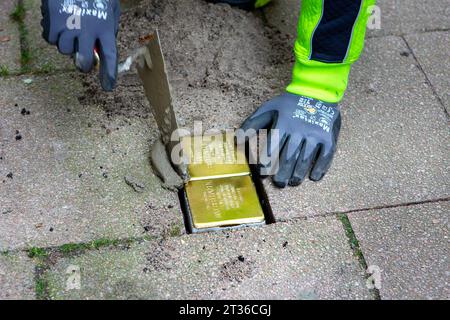 Wiesbaden, Germany - October 17, 2023: A bricklayer lays Stolpersteine on a pavement in the city center of Wiesbaden, Germany. A Stolperstein (literally 'stumbling stone') is a concrete cube provided with a brass plate inscribed with the name and life dates of victims of Nazi extermination. Stock Photo