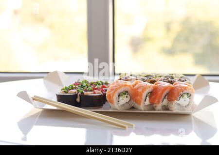Tasty sushi rolls in disposable paper box on white table. Delivery service Japan food in eco container concept Stock Photo