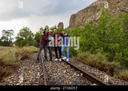 Happy friends standing on railroad tracks amidst plants Stock Photo