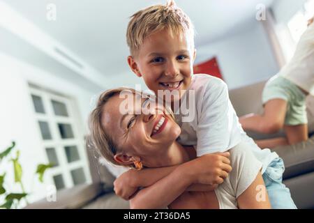 Smiling boy hugging mother in living room Stock Photo