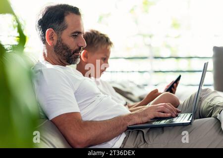 Man working on laptop by son sitting in living room Stock Photo