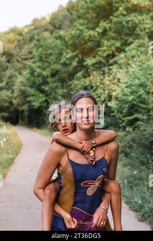 Happy mother giving piggyback ride to son in forest Stock Photo