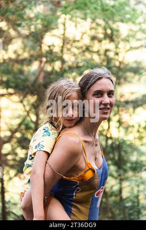 Smiling mother giving piggyback ride to son in forest Stock Photo