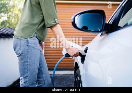 Woman wearing jeans charging electric car at station Stock Photo