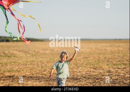 Happy boy flying kite and running in meadow Stock Photo