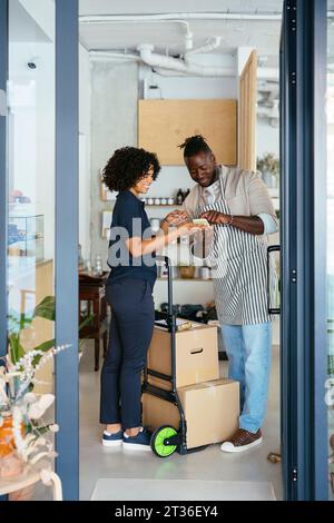 Smiling waiter and delivery woman using smart phone in cafe Stock Photo