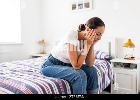 Sad woman with head in hands sitting on bed at home Stock Photo