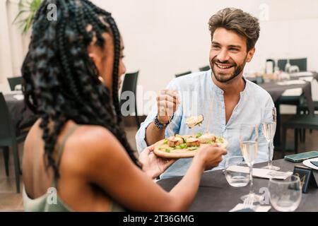 A smiling young man shares a meal with a woman at a contemporary dining setting, highlighting a relaxed and enjoyable lunch date. Best friends enjoyin Stock Photo