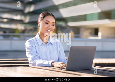 Smiling korean young business lady using laptop in urban area Stock Photo