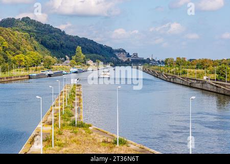Boat sailing through canal towards Lanaye lock, boats on shore, mountains part of nature reserve in Belgian part of Sint-Pietersberg with green trees Stock Photo