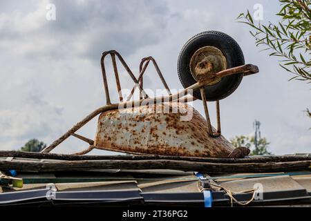 Old rusty white metal wheelbarrow upside down abandoned on wooden planks on deck of a ship against gray cloud covered sky in background, cloudy summer Stock Photo