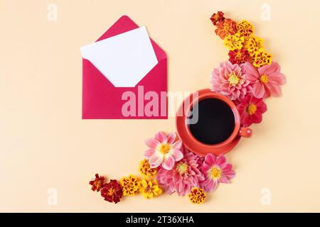 Burgundy envelope with a white blank sheet of paper for text, an orange cup of black coffee and orange marigold, dahlia flowers on orange background. Stock Photo