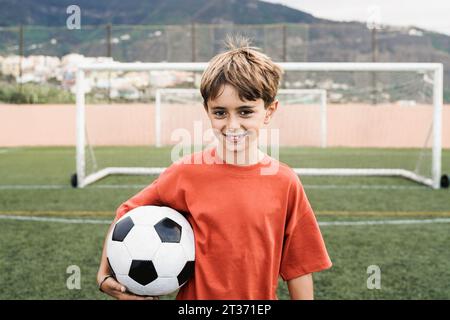 Child boy soccer player holding ball with football field on background - Children sport life style Stock Photo