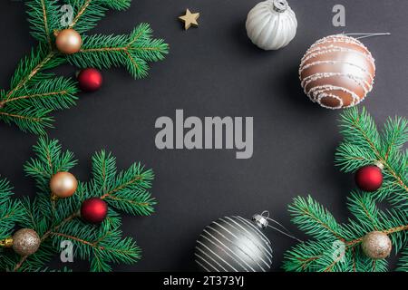Christmas frame made of fir branches with Christmas balls on black background. Top view, flat lay, copy space. Stock Photo