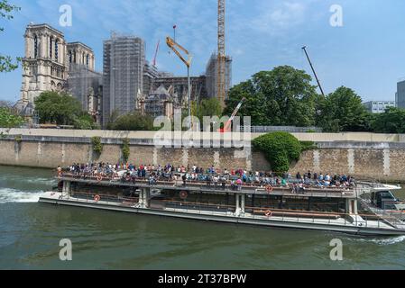 Notre Dame scaffolded, rebuilding after the fire, in front an excursion boat with tourists on the Seine, Paris, France Stock Photo