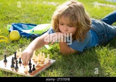 Chess school outdoor. Child laying on grass in spring park and think about chess game. Child education concept. Intelligent, smart and clever school k Stock Photo