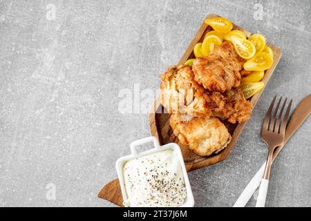 The fish dish is fried cod fillet with a creamy sauce and yellow plum tomatoes, served on a fish-shaped wooden platter. top view, Copy space Stock Photo