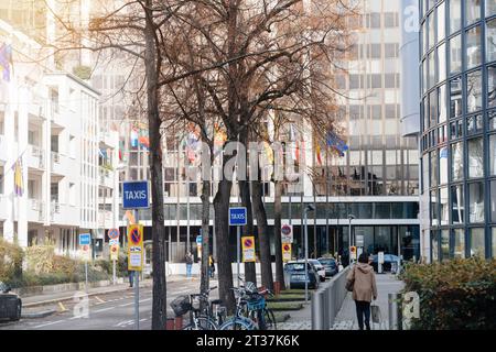 Strasbourg, France - Nov 22, 2023: A taxi sign stands prominently along the street, with the Winston Churchill building of the European Parliament in the background. A pedestrian woman can be seen walking nearby, adding life to the urban scene Stock Photo