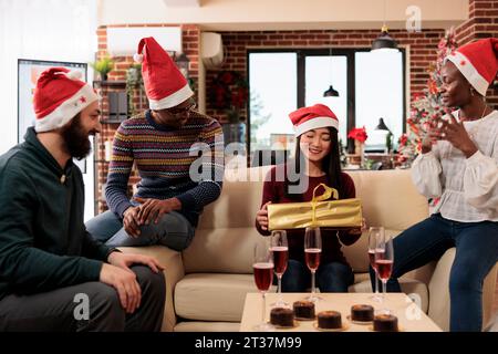 Smiling asian woman worker receiving present from coworkers while celebrating christmas in office together. Company employee holding festive wrapped box while sharing gifts with colleagues team Stock Photo