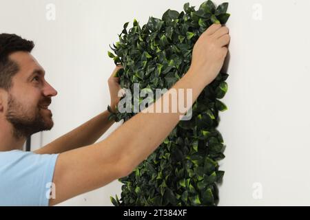Man installing green artificial plant panel on white wall in room Stock Photo