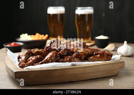 Tasty chicken wings, sauces, vegetable sticks and glasses of beer on wooden table, closeup. Delicious snacks Stock Photo