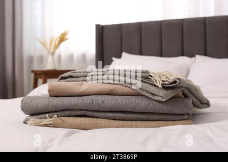 Stack of different folded blankets on bed in room. Home textile Stock Photo