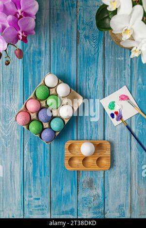 Multicolored easter eggs on blue table with paint brushes and paint Stock Photo