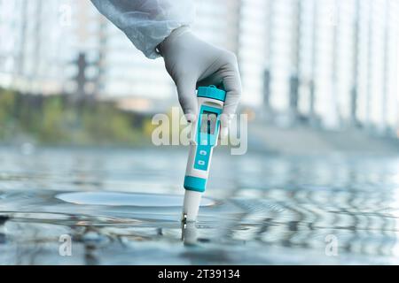 Electronic water testing hand over blurred blue swimming water background, water quality check. testing the level of water pollution in a natural rese Stock Photo