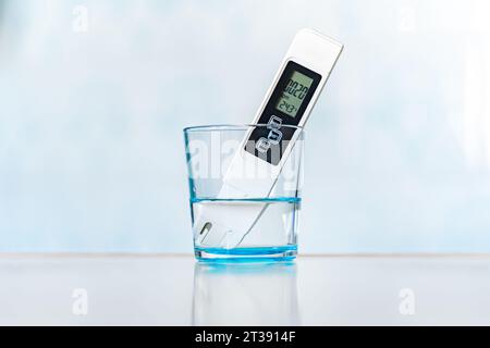 Water quality meter tester submerged in drinking glass, on blue background. Measuring harmful impurities, distilled water, purifying water for healthy Stock Photo