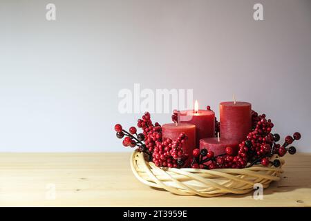 First advent with four red candles, one of them lighted, in a natural willow wicker wreath with berry decoration, seasonal home decor, copy space, sel Stock Photo