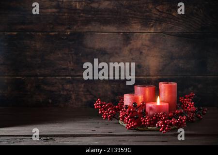 Frist Advent with red berry decoration and candles in a wreath, one is lighted, holiday home decor against a dark rustic wooden background, copy space Stock Photo