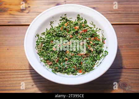 Taboule, Lebanese parsley salad with tomatoes, onions and mint in a white bowl on a rustic wooden table, seen from above, copy space, selected focus, Stock Photo