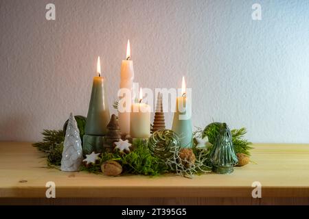 Fourth Advent, decoration with four different lit candles, some moss, green Christmas balls from glass and cinnamon stars on a wooden sideboard agains Stock Photo