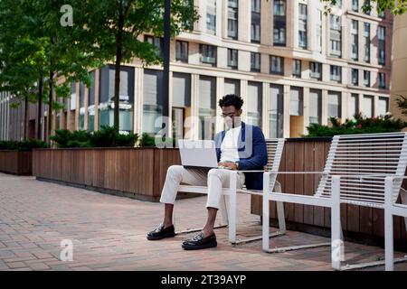 Black man with laptop who works on street near city business center. Fashionable businessman outdoors. Stock Photo