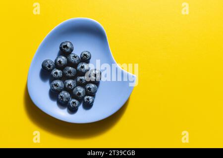 Fresh blueberries presented on a blue vintage plate and isolated on a yellow background. Stock Photo