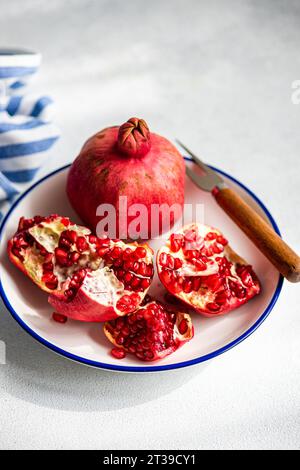 A ripe pomegranate open on a blue-trimmed plate, revealing its red seeds, accompanied by a wooden handled knife.. Stock Photo