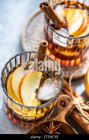 Fresh apple cider cocktails garnished with cinnamon sticks, star anise, and apple slices in a crystal glass filled with ice cubes on a textured backgr Stock Photo