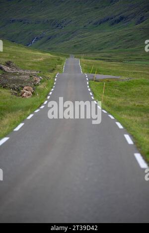 Picturesque view of empty asphalt roadway running through green valley towards mountain slope in Faroe Islands during road trip Stock Photo