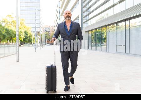 Businessman walking down the street with his suitcase while looking away Stock Photo