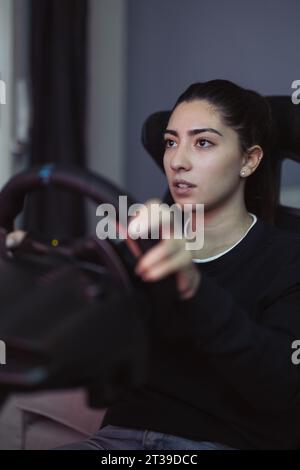 Portrait of serious young female in casual clothes holding console steering wheel while playing car racing game at home during weekend Stock Photo