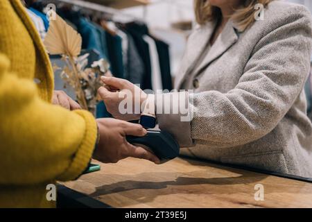 Close-up of a customer making a contactless payment to a store owner using a smartwatch. Stock Photo