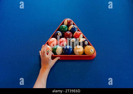 Top view of crop anonymous person placing colorful pyramid of billiard balls in billiard triangle on blue pool table Stock Photo