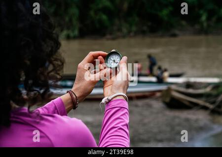 Back view of crop anonymous female traveler in casual clothes holding vintage compass in hands against blurred background of people in boats in Amazon Stock Photo