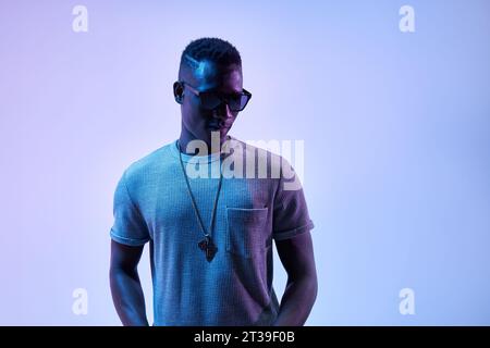 Young African American man with a trendy haircut and sunglasses stands confidently against a purple Stock Photo
