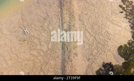 Aerial top view of white paddleboat floating on clear ocean water with rough sand on sunny summer day in El Rompido Stock Photo